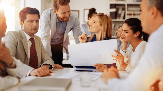 Employees gathered at a table looking at a piece of paper together, smiling and talking